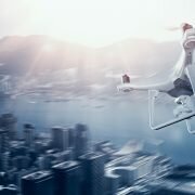 Photo White Matte Generic Design Remote Control Air Drone with action camera Flying Sky under City. Modern Megapolis Background. Wide, side angle view. Motion blur Effect. 3D rendering.